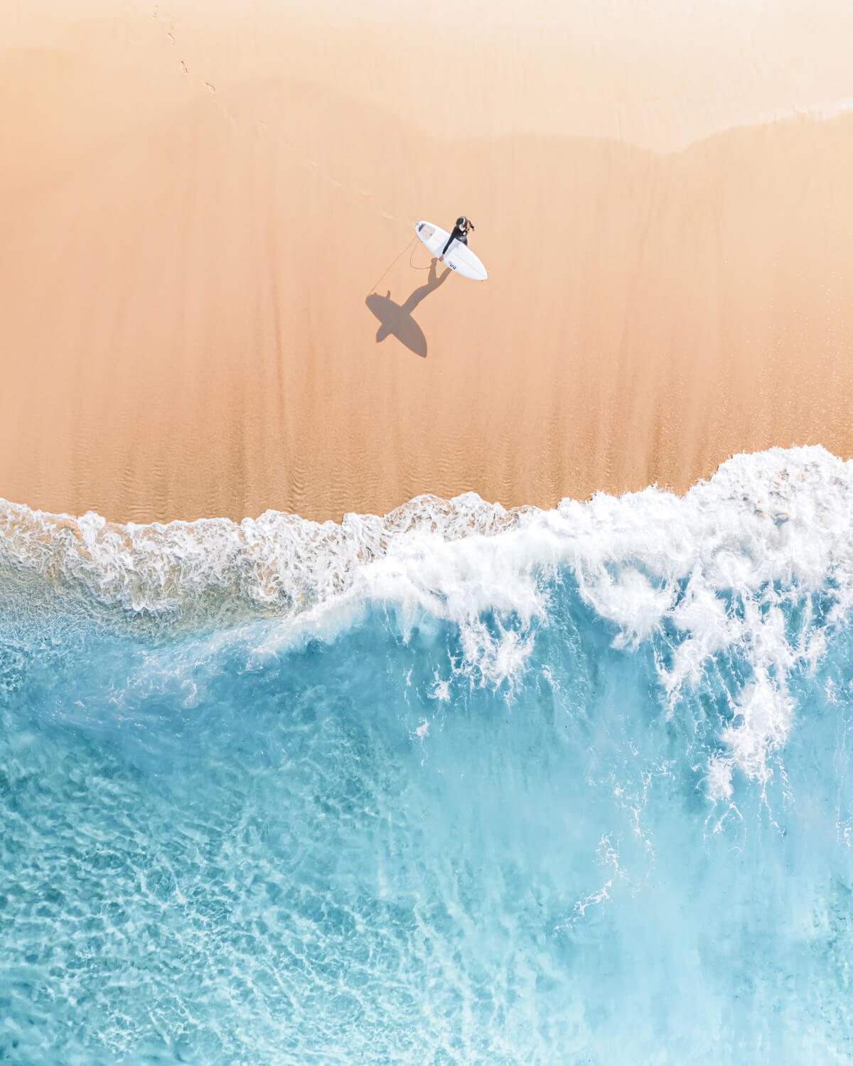 A Beach Photography taken from above of a surfer walking toward the ocean