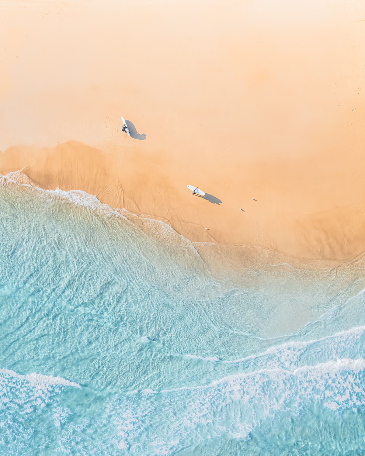 Aerial view of The Pass in Byron Bay, showing surfers with surfboards on the beach and gentle ocean waves.