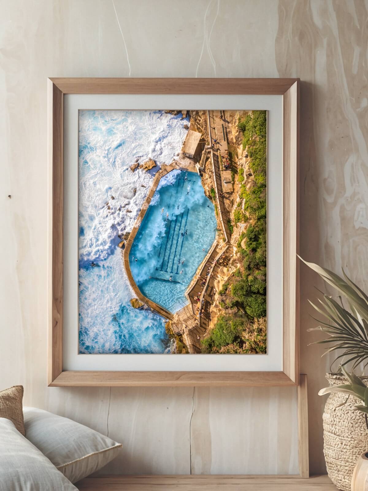 Framed aerial view of Bronte Ocean Pool with crashing waves and surrounding rocky coastline.