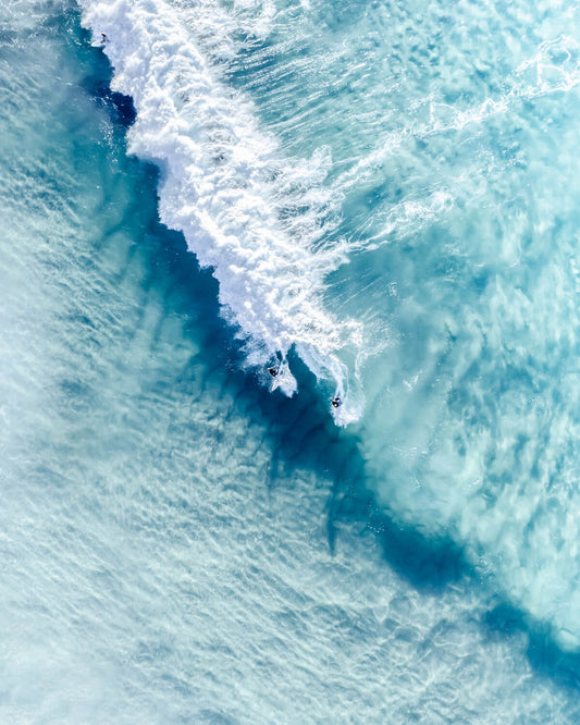 Aerial view of twin surfers riding a wave in Bondi Beach’s turquoise waters.