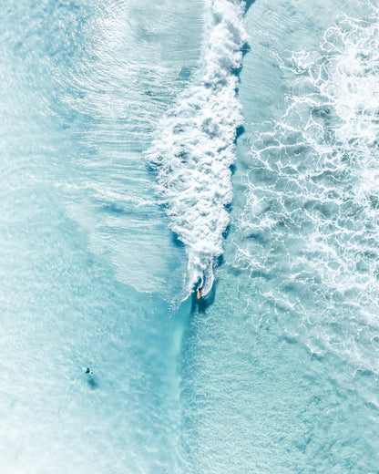 Aerial view of surfers riding waves in Byron Bay at The Pass with blue ocean tones.