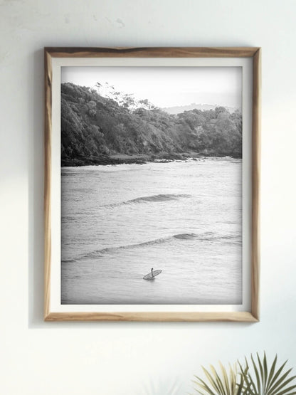 Framed black-and-white art print of a surfer at Wategos Beach, Byron Bay, displayed in a cozy modern room.