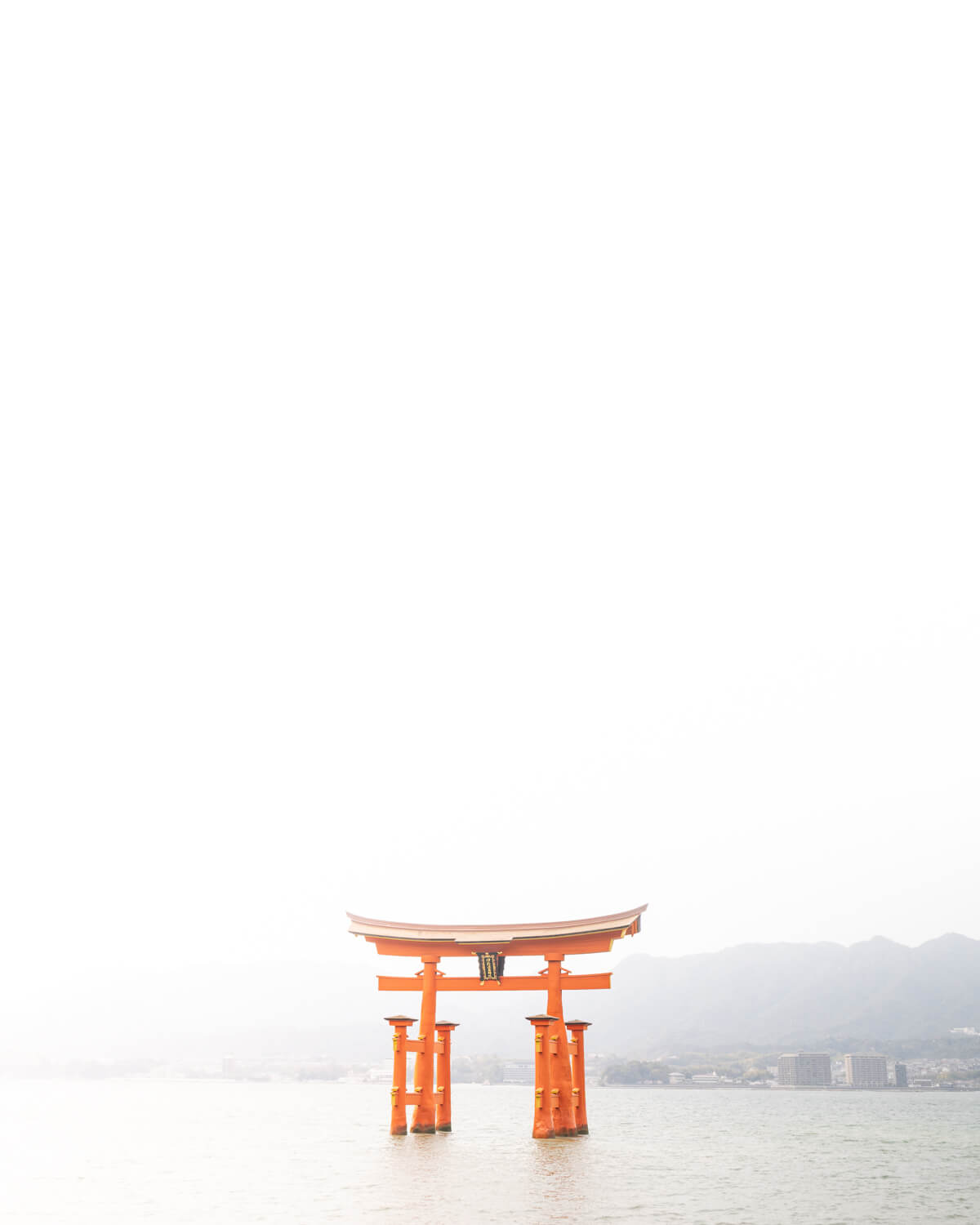 Itsukushima Shrine’s Torii Gate standing above water in Miyajima, Japan, shrouded in mist.