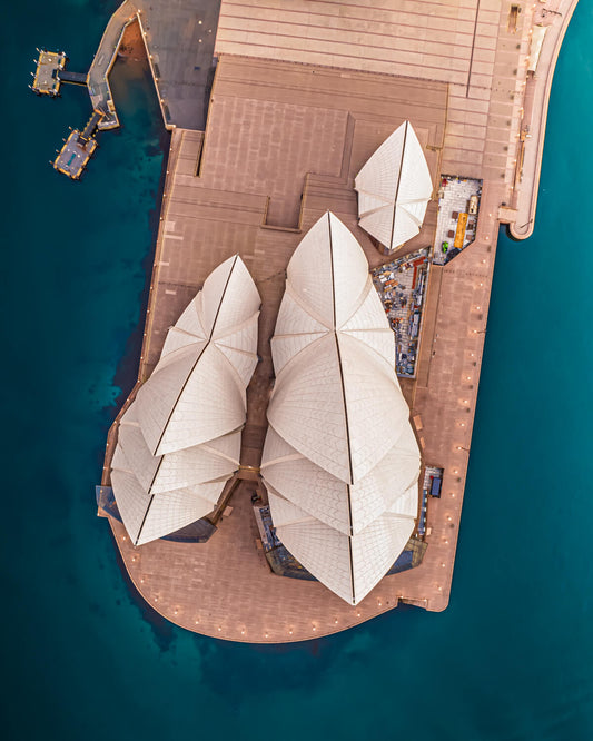 Drone shot of Sydney Opera House from above, capturing its iconic sail-like architecture against the deep blue waterfront.