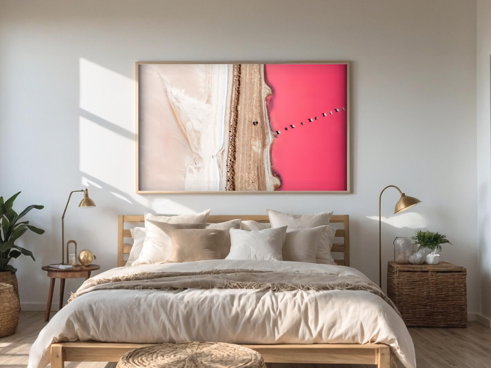 A bedroom with a huge frame above it presenting the Pink lake photo.