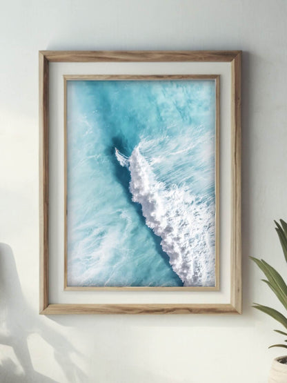 Framed aerial view of a surfer riding a vibrant ocean wave with splashing foam.