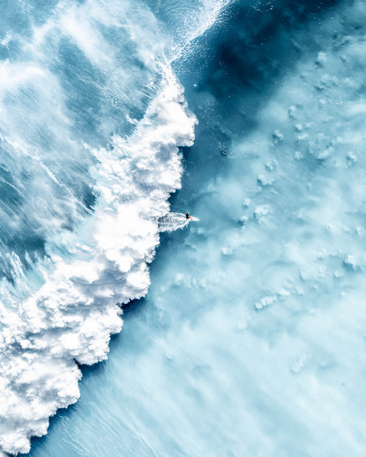 Surfer riding a powerful wave at Bronte Beach in an abstract aerial view with vivid blue tones