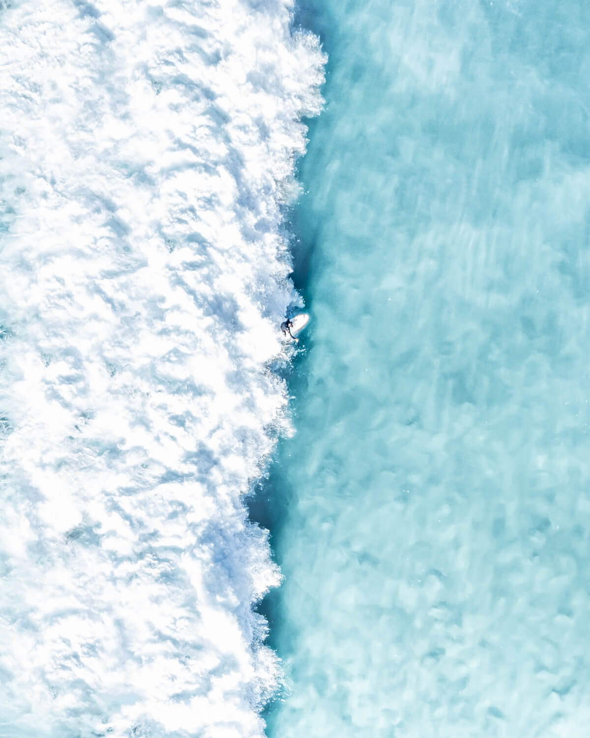 Aerial view of a surfer riding a powerful wave at Bronte Beach, contrasting blue ocean and white frothy surf