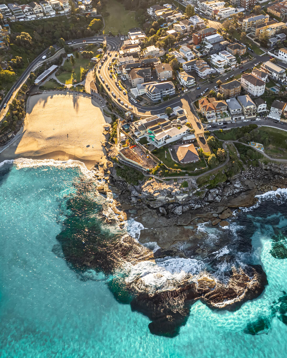 Tamarama Beach in Sydney with turquoise waters meeting golden sands, captured from above at sunset.